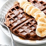 side angle view of chocolate vegan buckwheat waffles with banana and syrup.