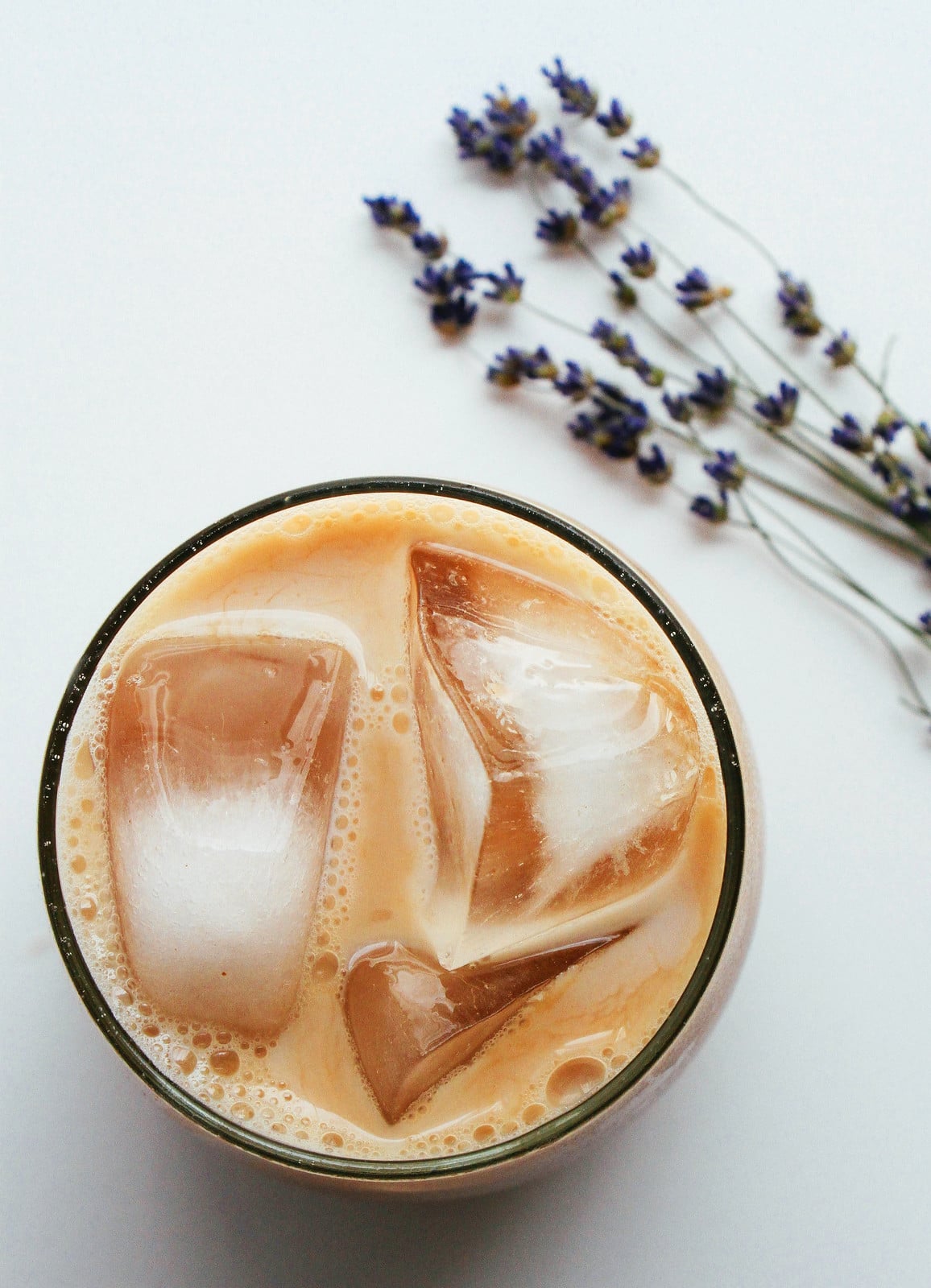 top down view of glass of lavender chai tea with large ice cubes.