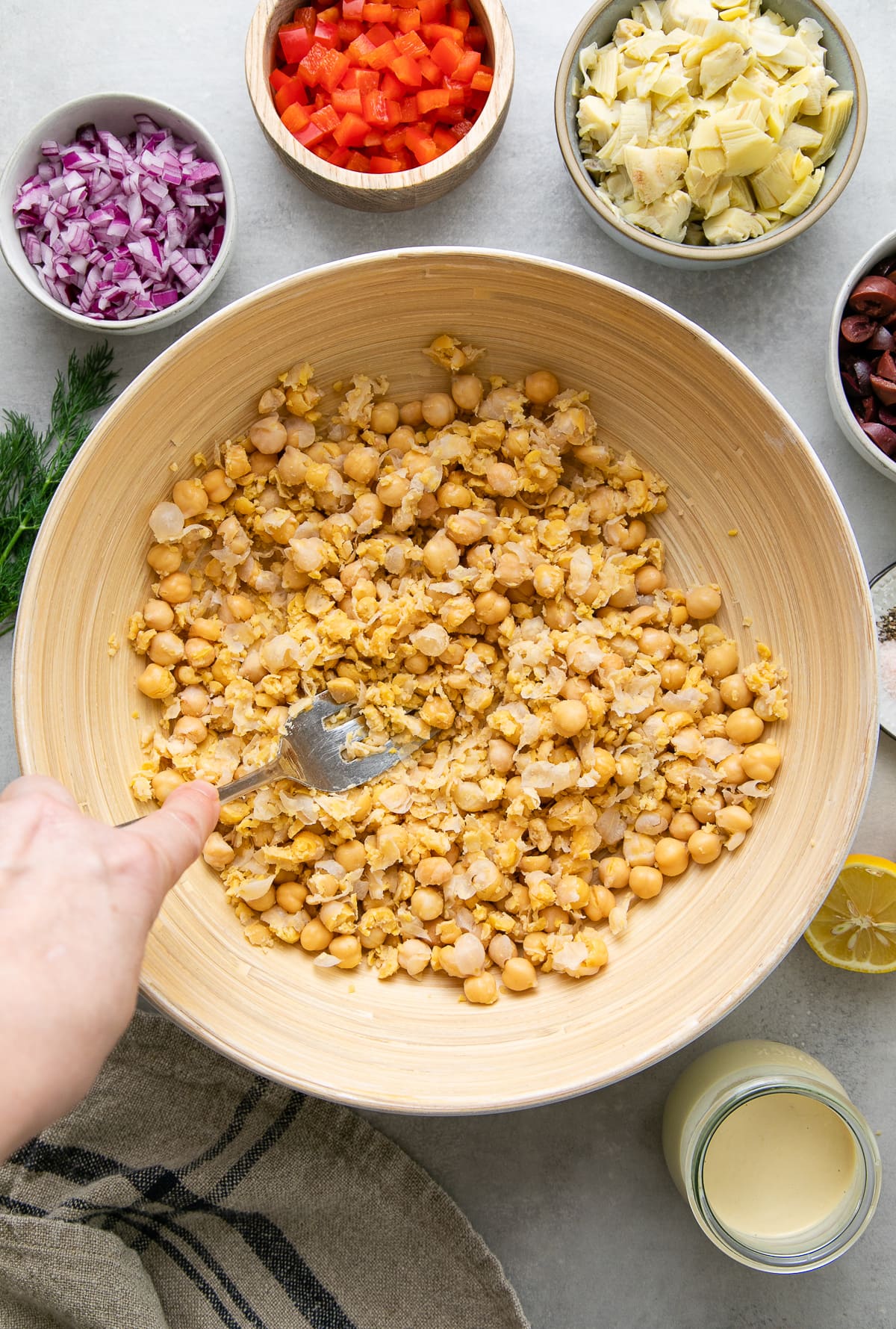 top down view showing the process of mashing chickpeas in a bowl with items surrounding.