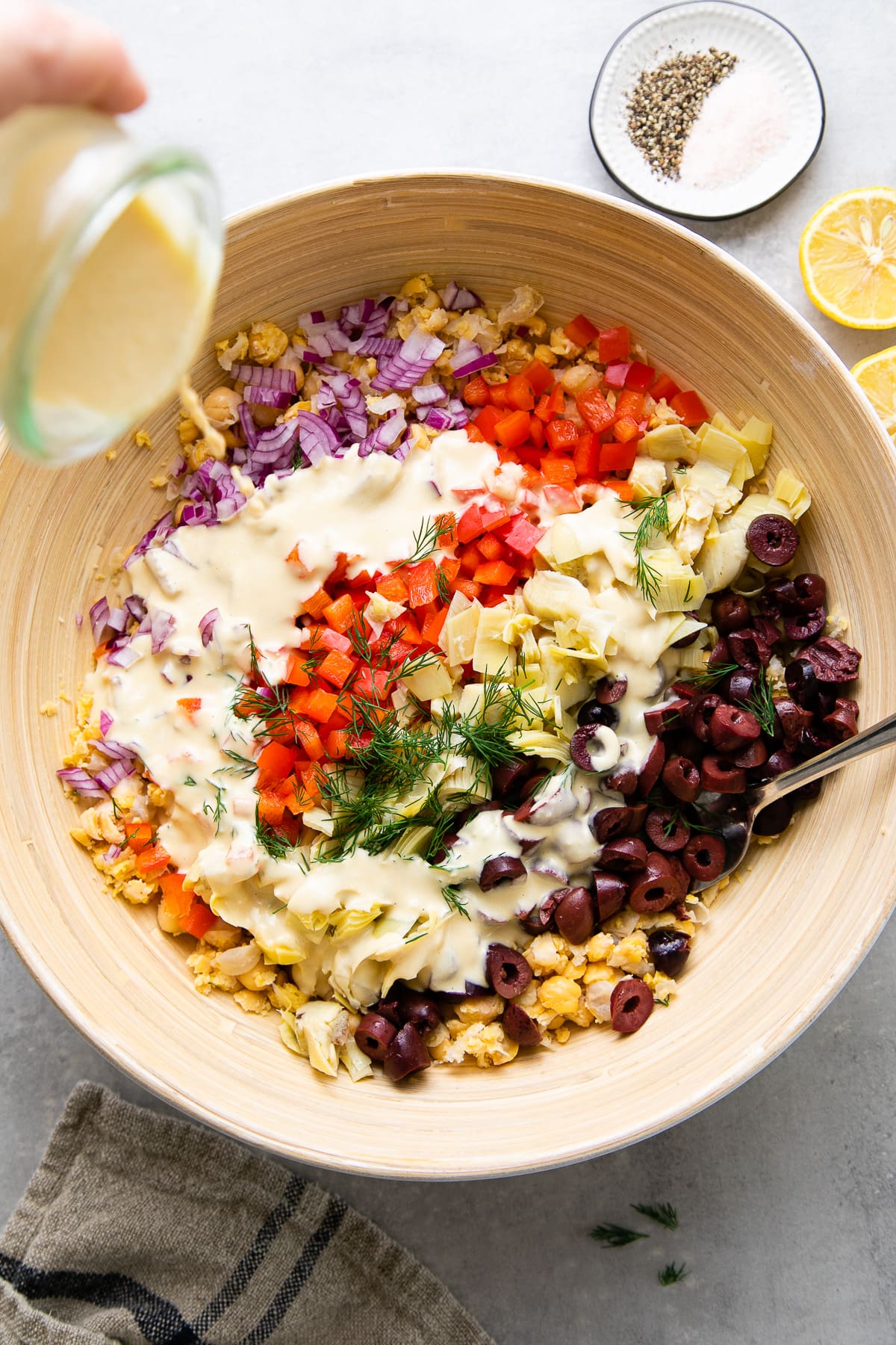 top down view showing the process of adding thinned hummus to salad ingredients.