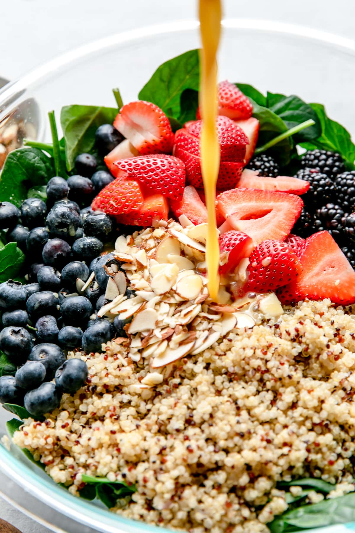 side angle view of orange dressing being poured over top berry spinach quinoa salad.