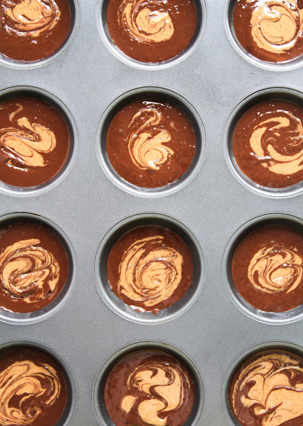 top down view of brownie batter added to muffin tin with nut butter swirl.