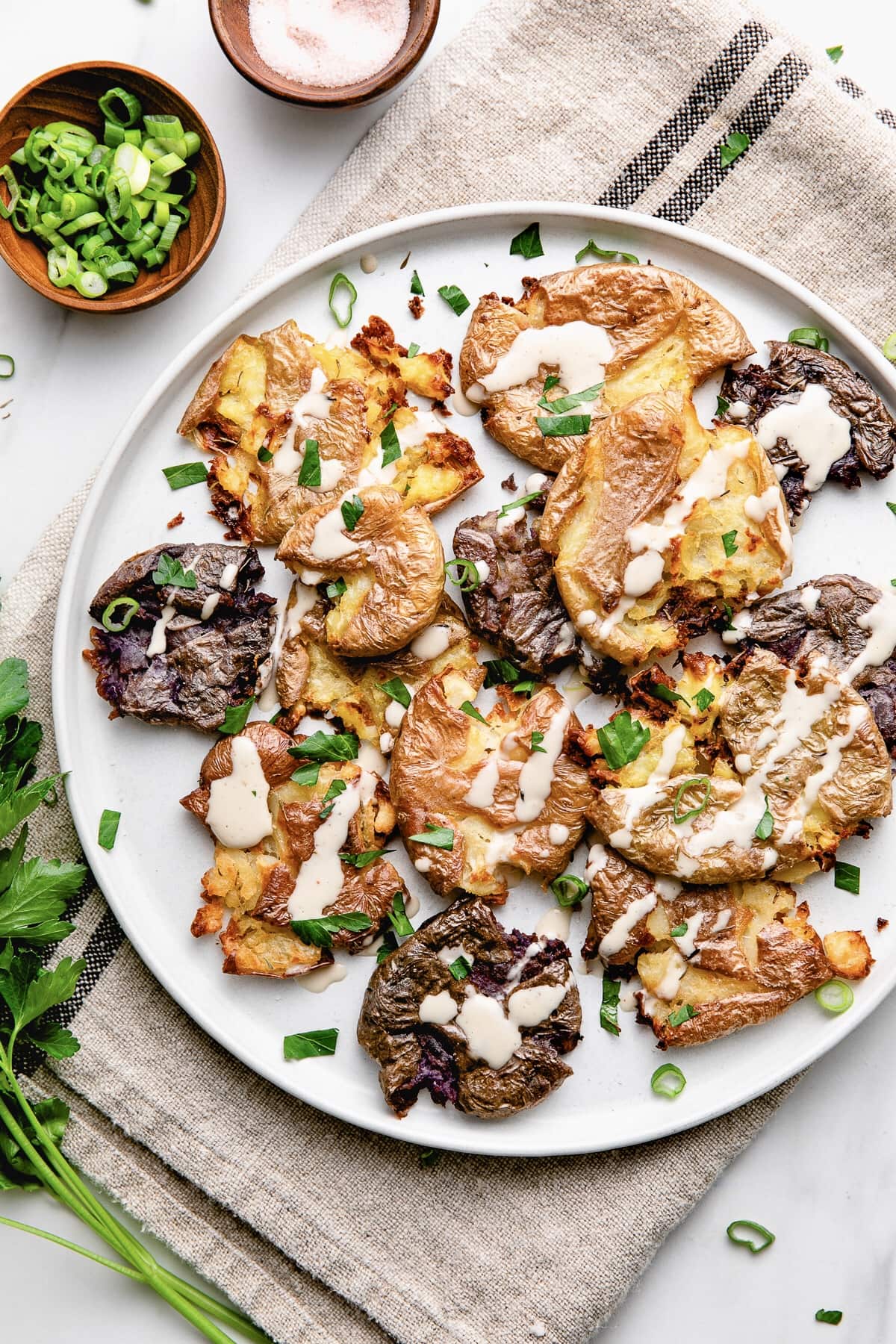 top down view of plated crispy smashed potatoes with tahini drizzle and items surrounding.