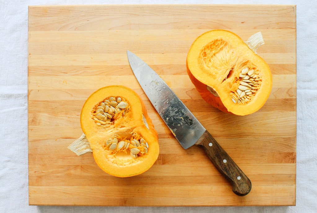 top down view of sugar pumpkin sliced in half on a cutting board.