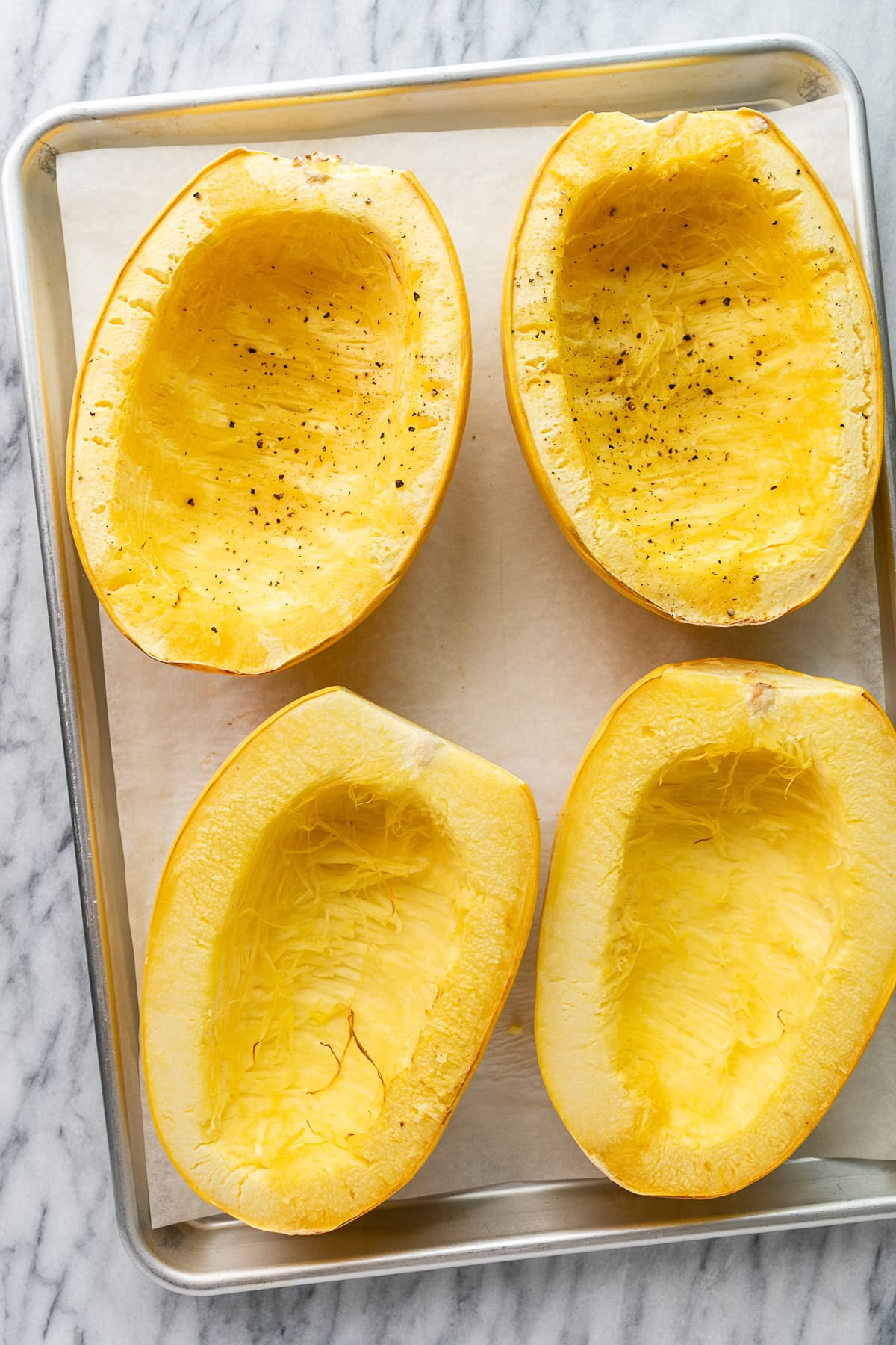 top down view of group of spaghetti squash halves freshly cooked in the oven on a metal sheet pan.