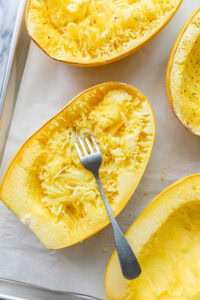 top down view of halved and baked spaghetti squash with fork on metal sheet pan.