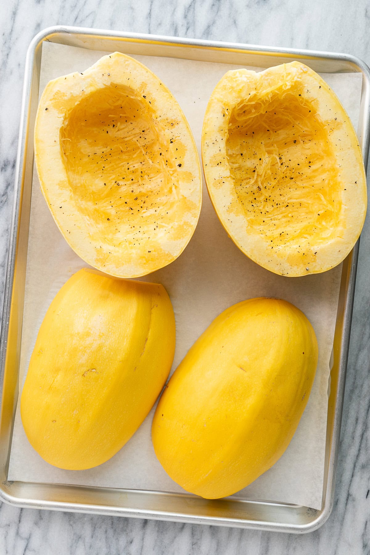 top down view of a group of halved spaghetti squash on metal baking sheet and ready for the oven.