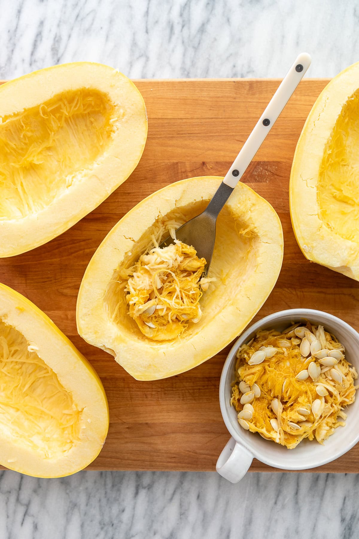 top down view of halved spaghetti squash with insides scooped out with spoon on a wooden cutting board.