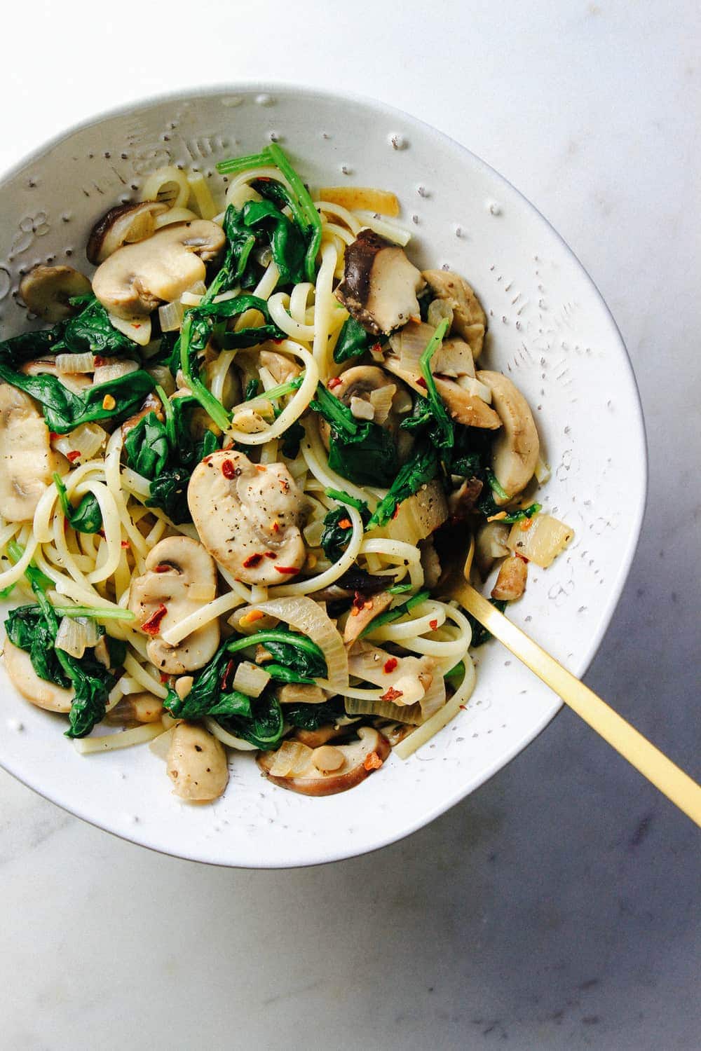 Garlicky Mushroom + Kale with Linquine in a white ceramic bowl with fork on marble countertop