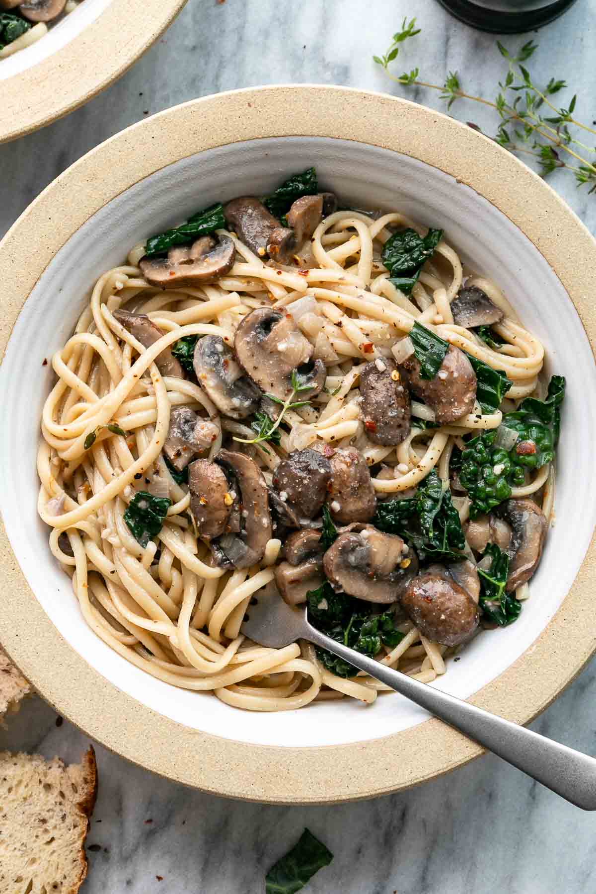 top down view of bowl with freshly made mushroom and kale pasta with items surrounding.