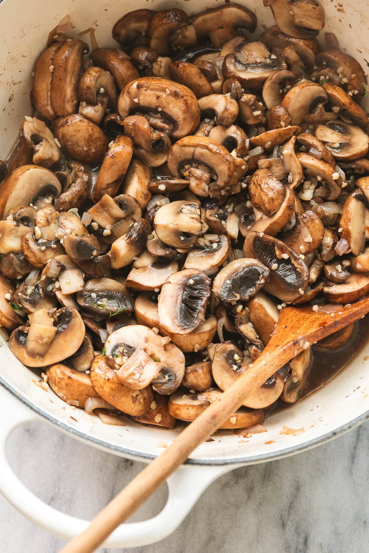top down view of sauteed mushrooms in a white pot with wooden spoon.