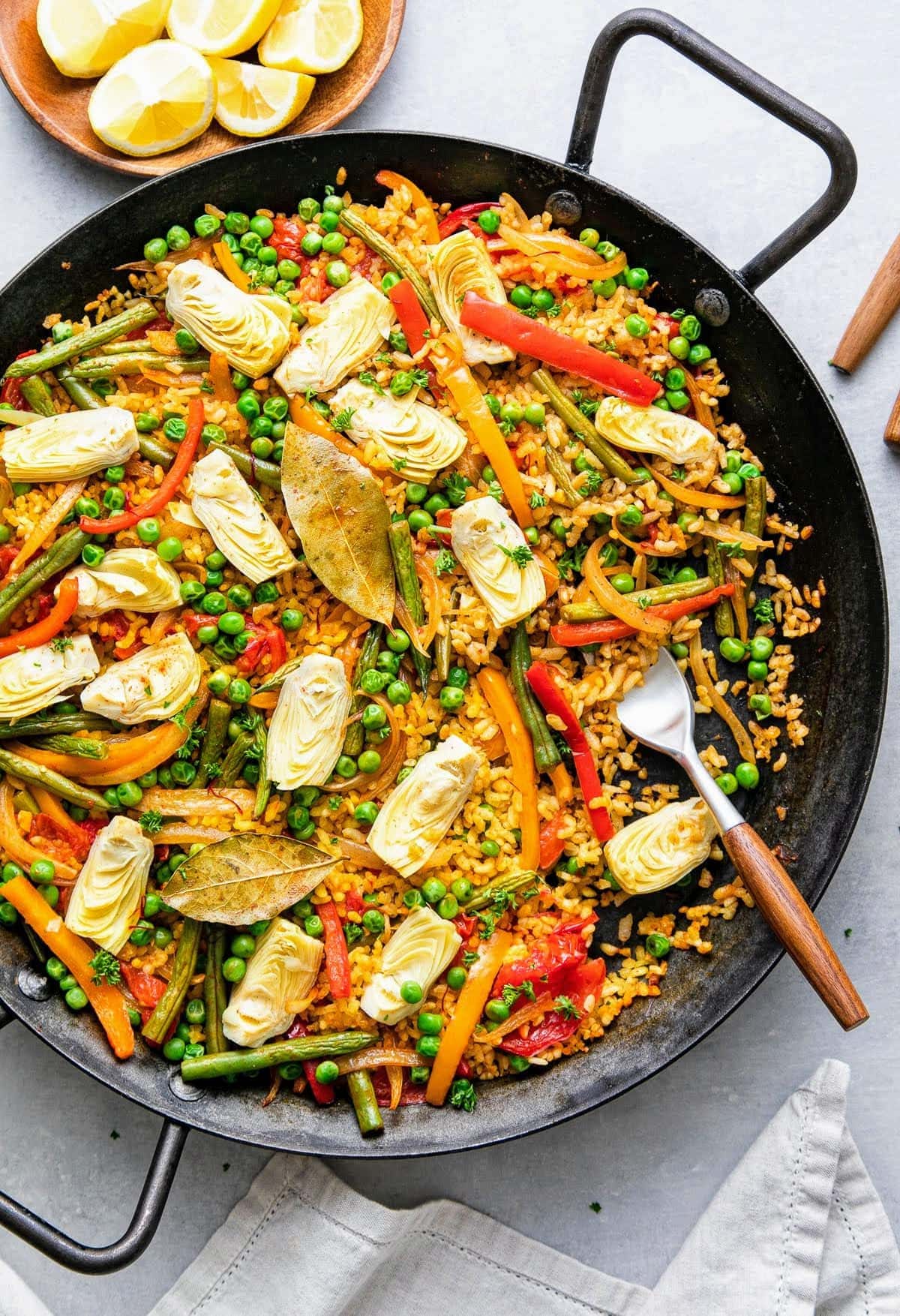 top down view of vegetable vegan paella in a paella pan with fork and items surrounding.