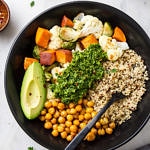 top down view of a black bowl with roasted veggies, chickpeas quinoa and chimichurri making a chimichurri nourish bowl.