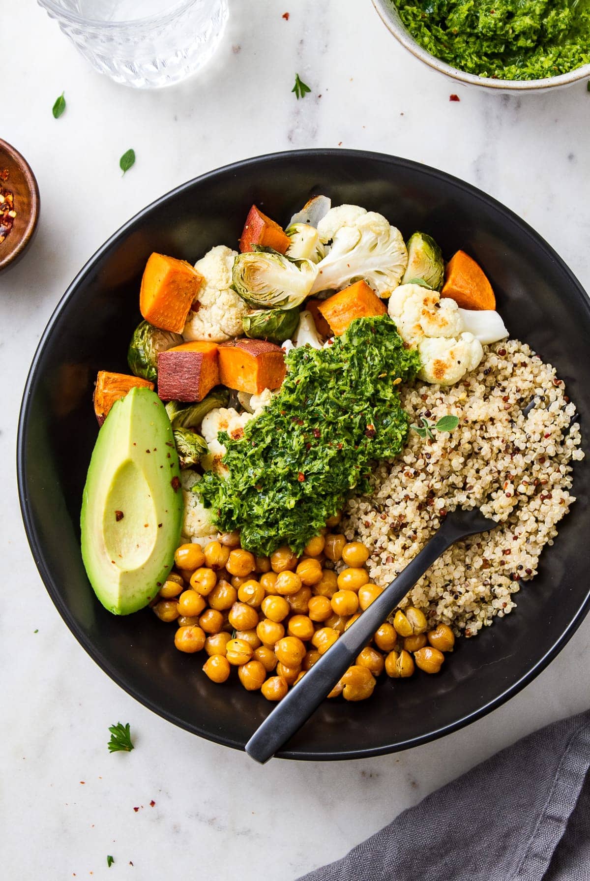 top down view of a black bowl with roasted veggies, quinoa, and chimichurri.