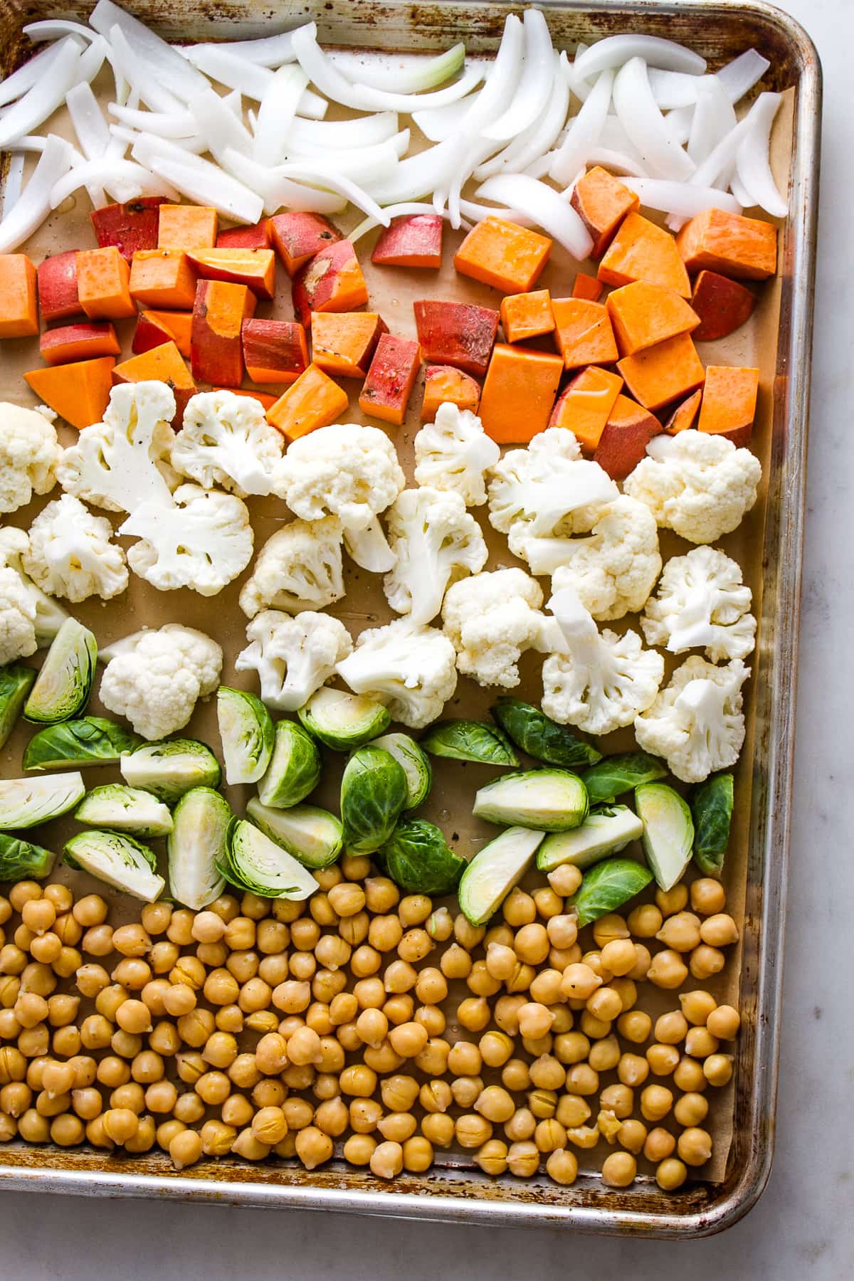top down view of prepped nourish bowl veggies on a baking sheet before being roasted.