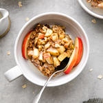 top down down of healthy apple baked oatmeal in a bowl with spoon and items surrounding.
