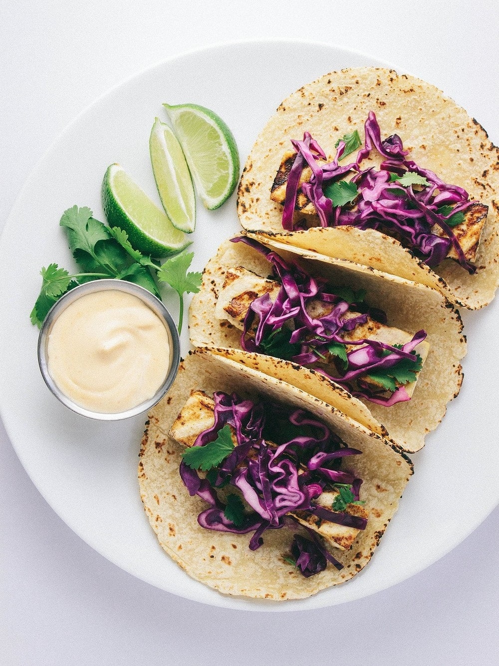 top down view of 3 grilled baja tofu tacos topped with red cabbage on a white plate