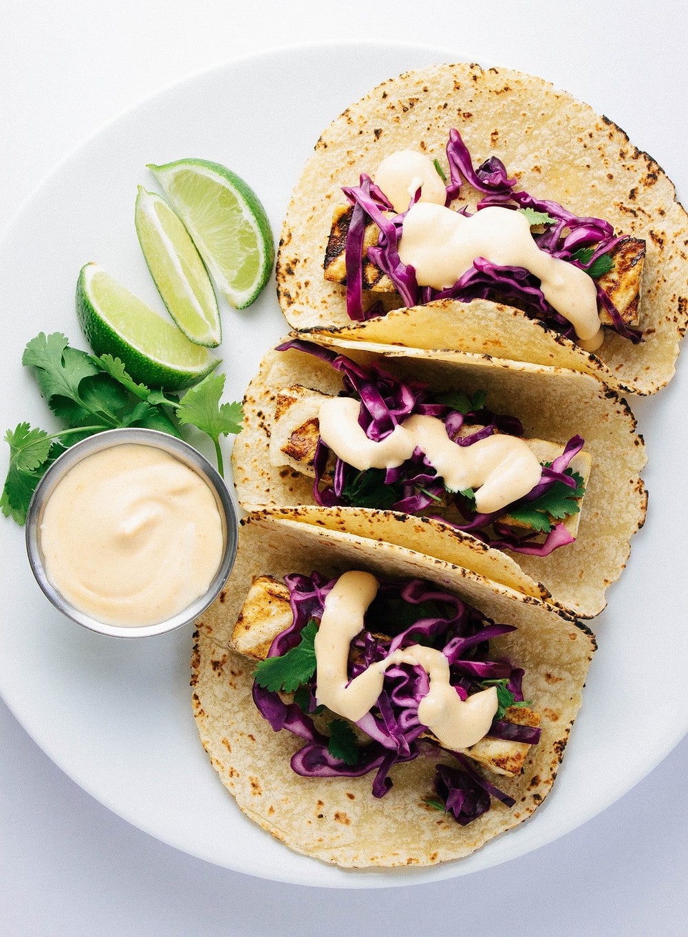 top down view of grilled baja tacos with creamy sauce on a white plate