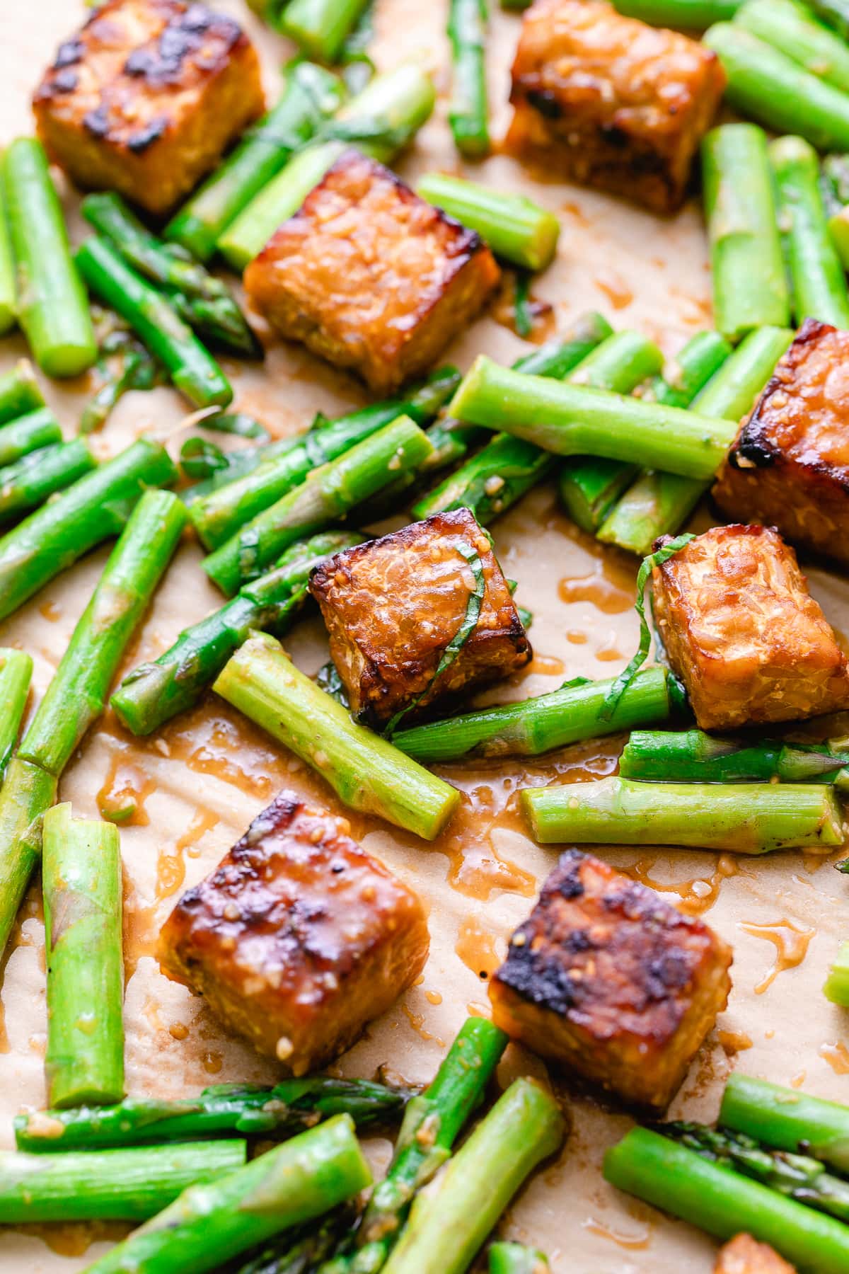 side angle view of baking sheet with fresh roasted orange miso tempeh and asparagus.