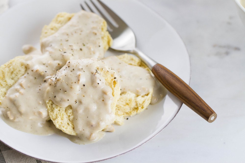 up close, side angle view of vegan biscuits smothered with gravy on a small with plate with fork with wooden handle. 