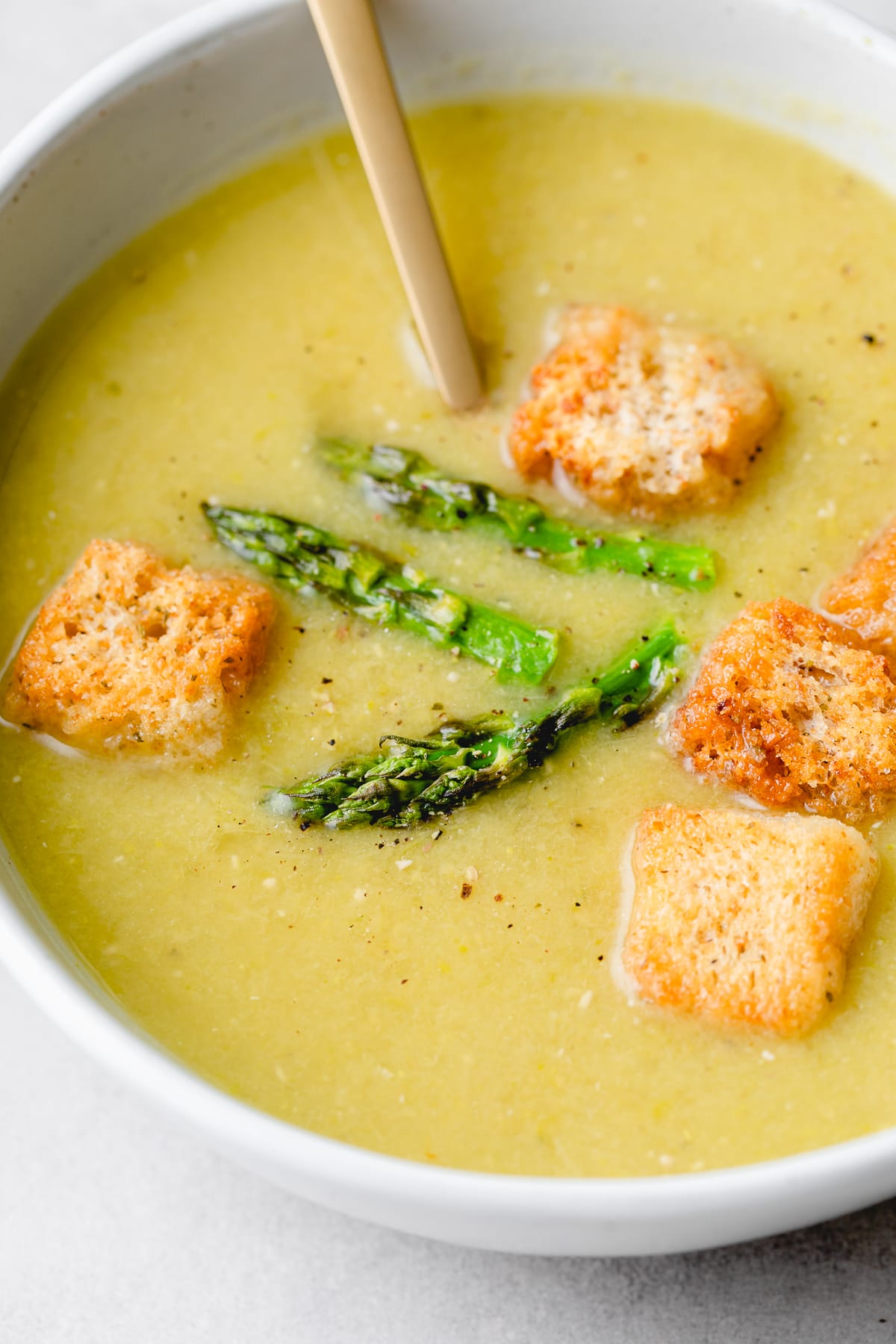 side angle view of bowl with vegan asparagus soup with spoon.