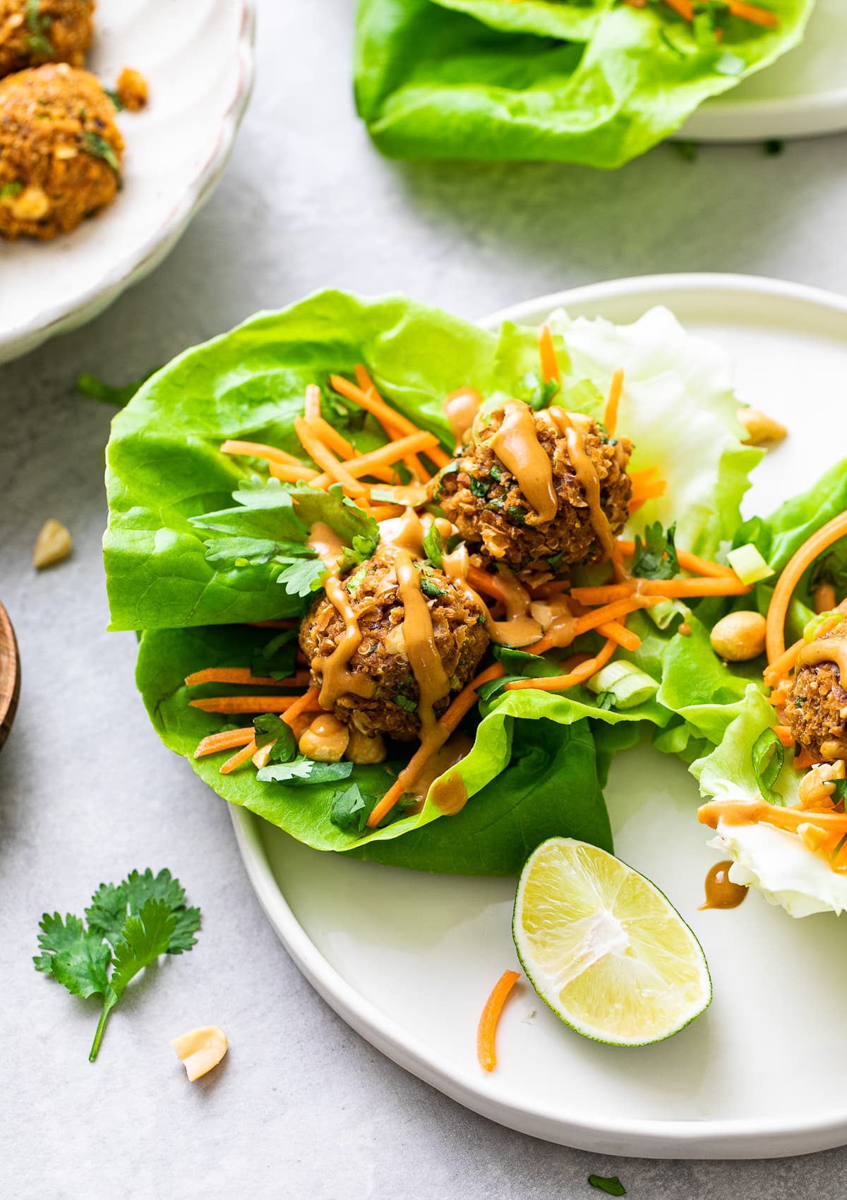 side angle view of vegan lettuce wraps with thai quinoa meatballs on a plate with items surrounding.