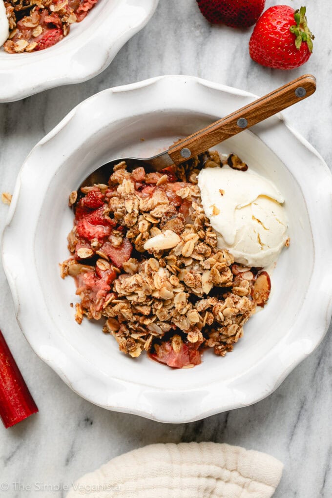 top down view of strawberry rhubarb crisp in a white bowl with vanilla ice cream and spoon.