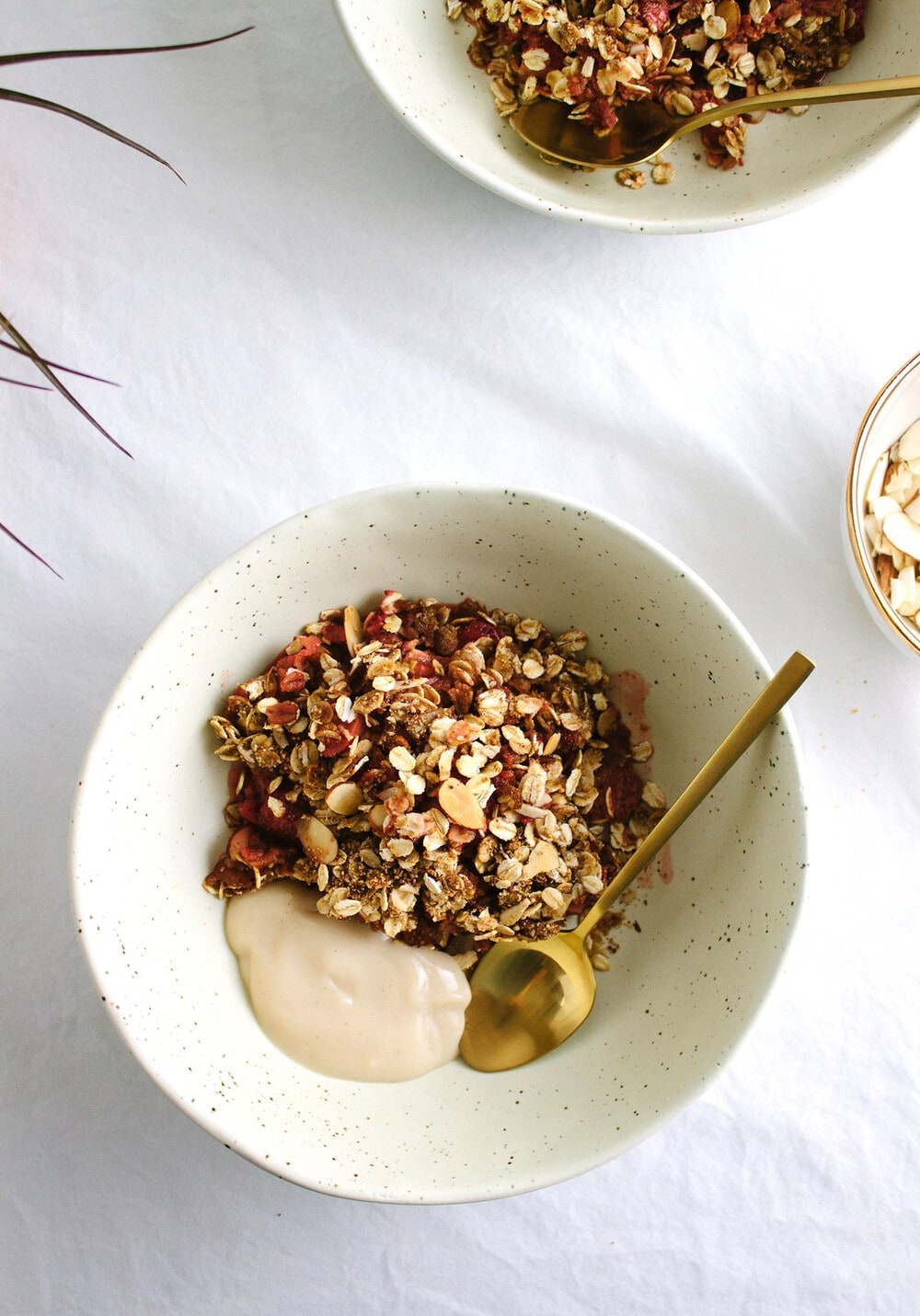 top down view of healthy strawberry rhubarb crisp in a bowl with vanilla yogurt and gold spoon.