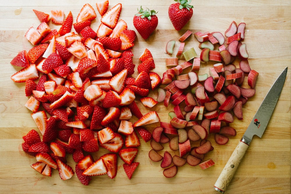 sliced strawberries and rhubarb on a wooden cutting board with a knife on a wooden cutting board.