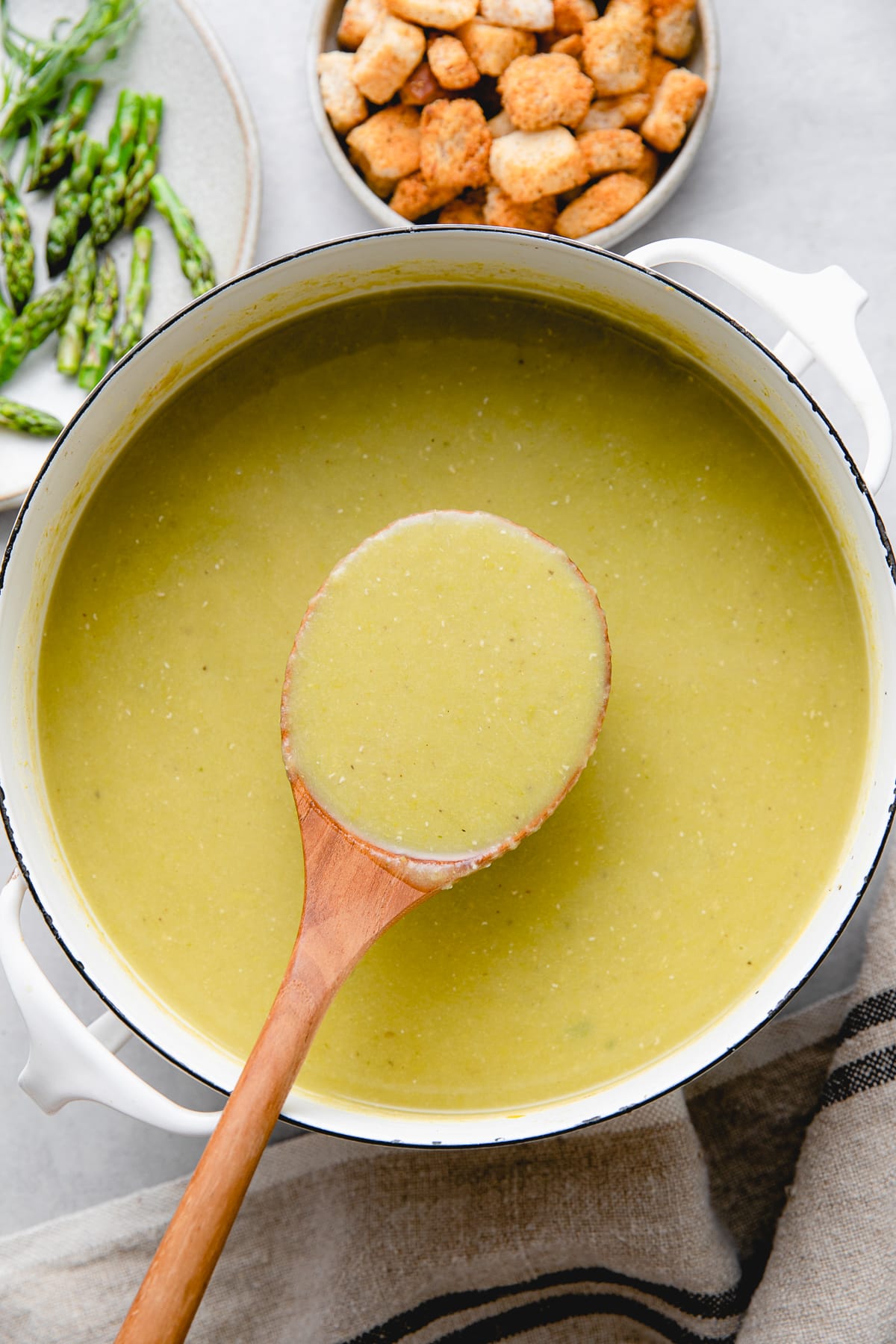 top down view of freshly made vegan asparagus soup in a pot with items surrounding.