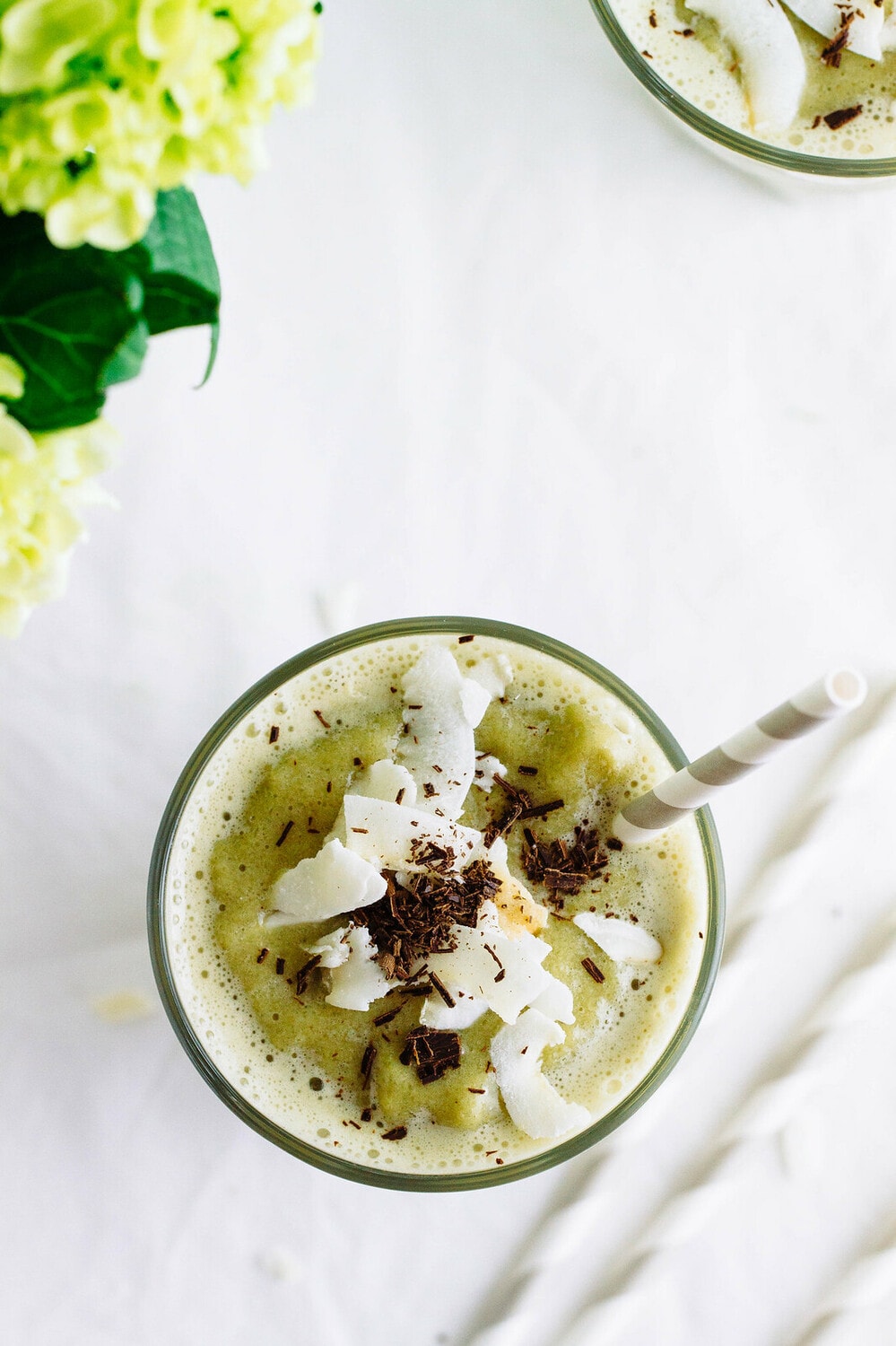 top down view of tasty vegan matcha shake in a glass with straw, topped with coconut and chocolate shavings.