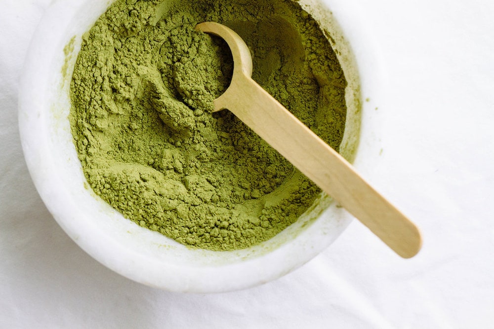 top down view of matcha powder in a small marble bowl with wooden spoon.