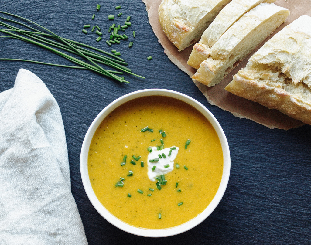 top down view of zucchini and sweet potato vichyssoise in a white bowl with items surronding.