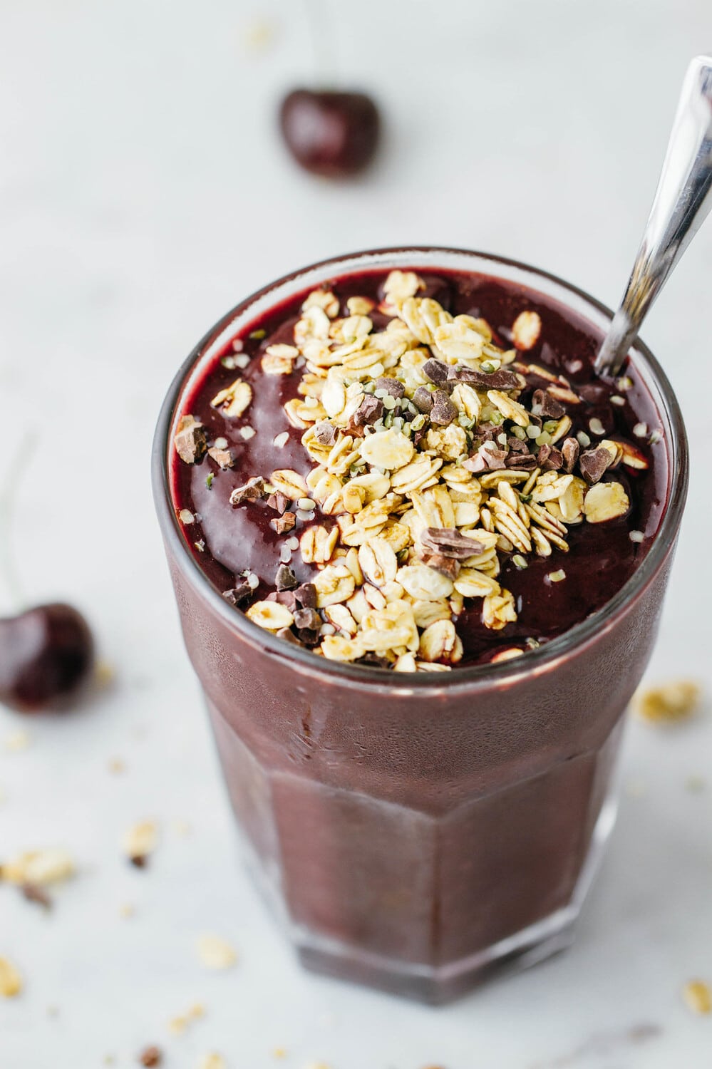 side angle view of a glass full of healthy and decadent chocolate cherry smoothie topped with granola.