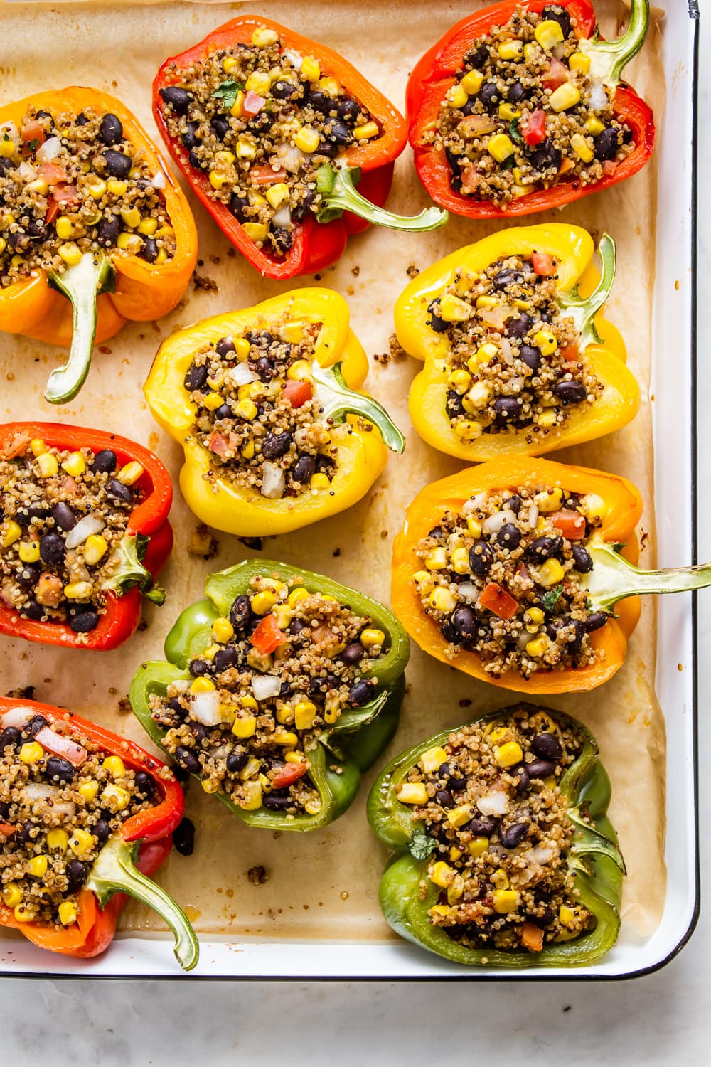 top down view of quinoa stuffed colored bell peppers on a rimmed baking sheet.