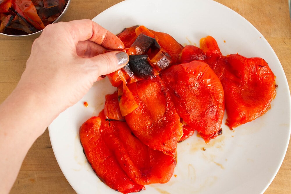 top down view of the skin of roasted red pepper being peeled from the flesh of steamed red pepper.