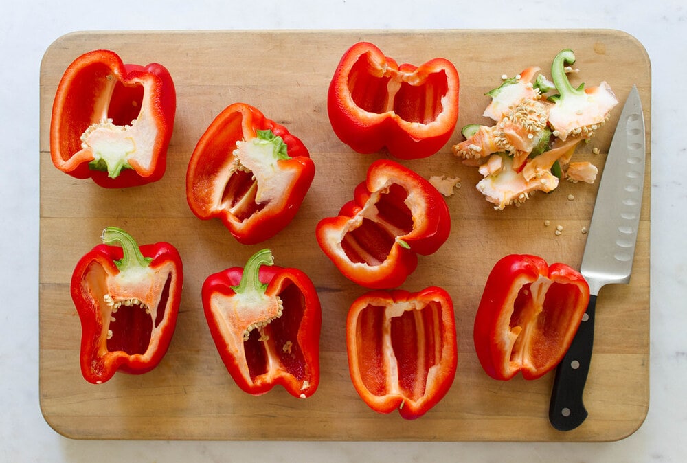 top down view of red bell peppers, cored, seeded and sliced in half lengthwise on a wooden cutting board.