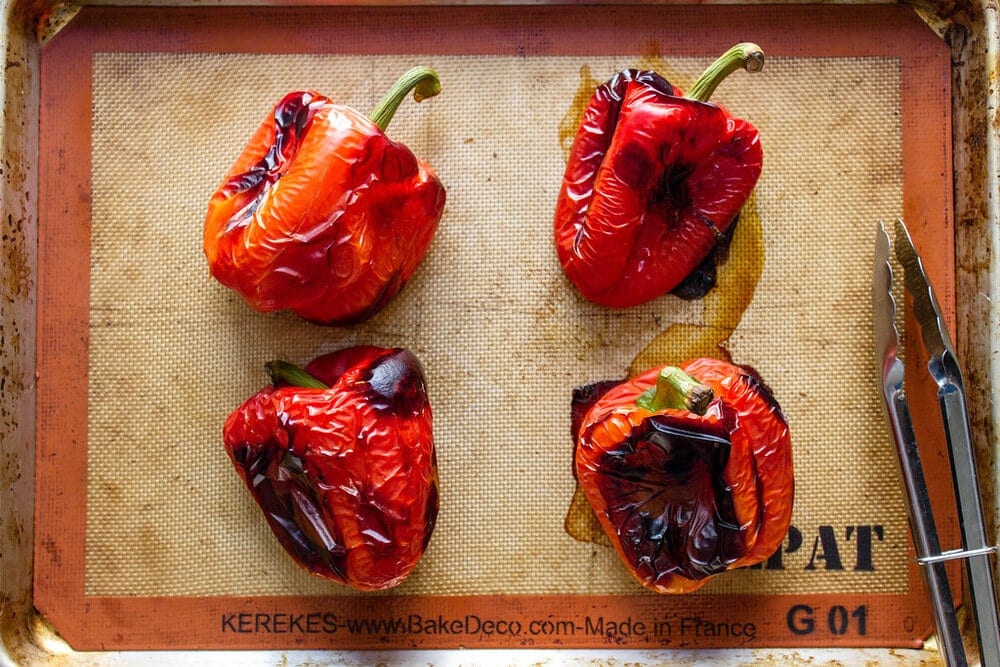 top down view of freshly roasted whole red peppers on a rimmed baking sheet.