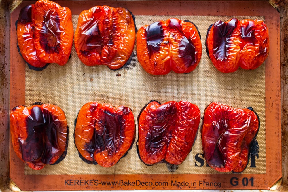 top down view of freshly oven sliced roasted red peppers on a rimmed baking sheet.