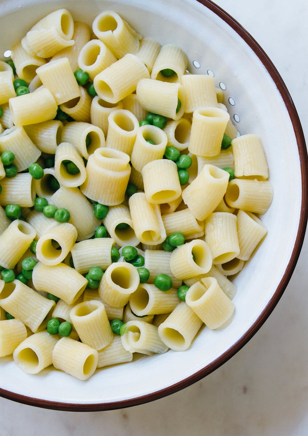 top down view of a white colander with freshly cooked pasta and peas.