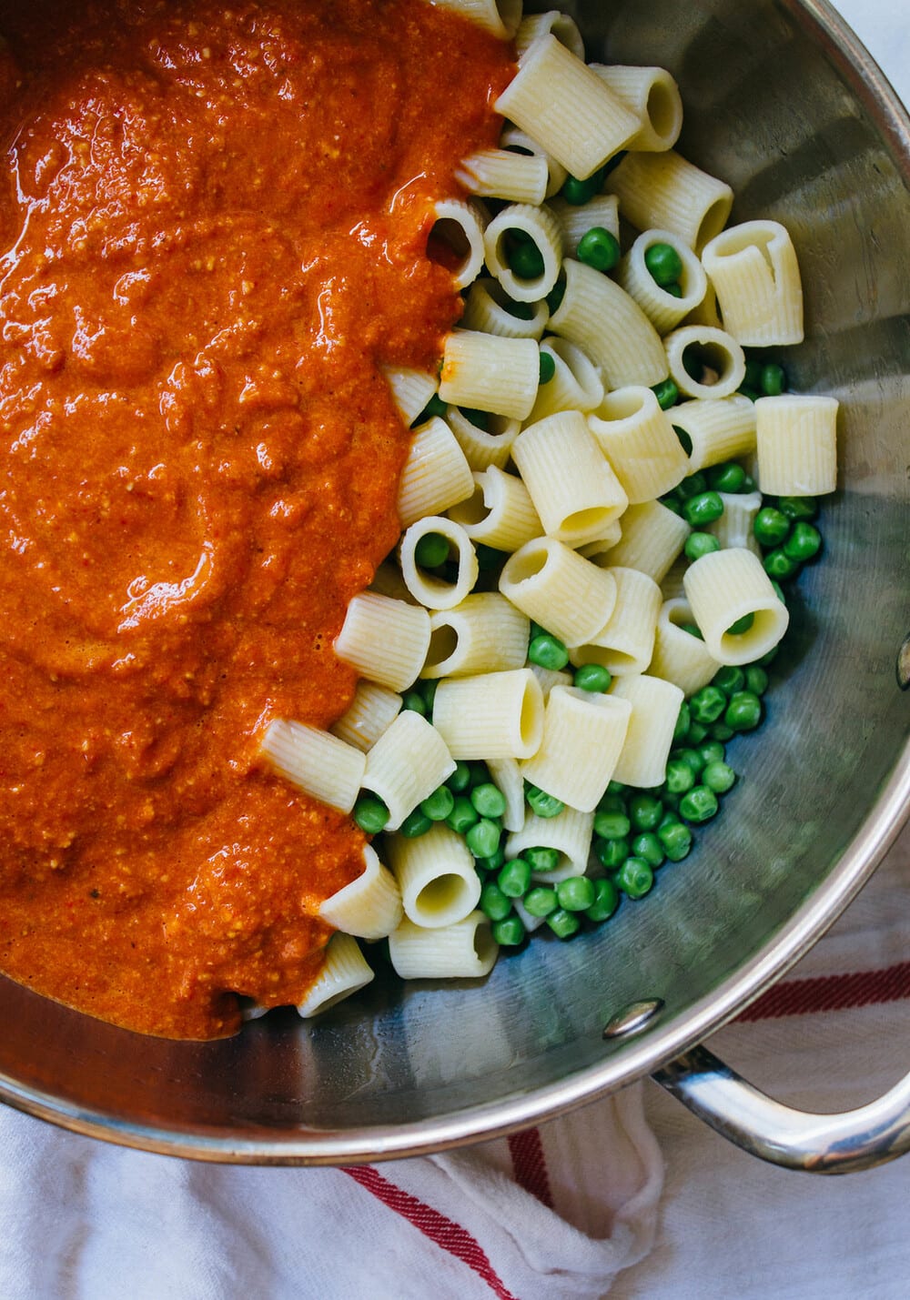 top down view of a pot with cooked pasta and peas, topped with romesco sauce before combining.