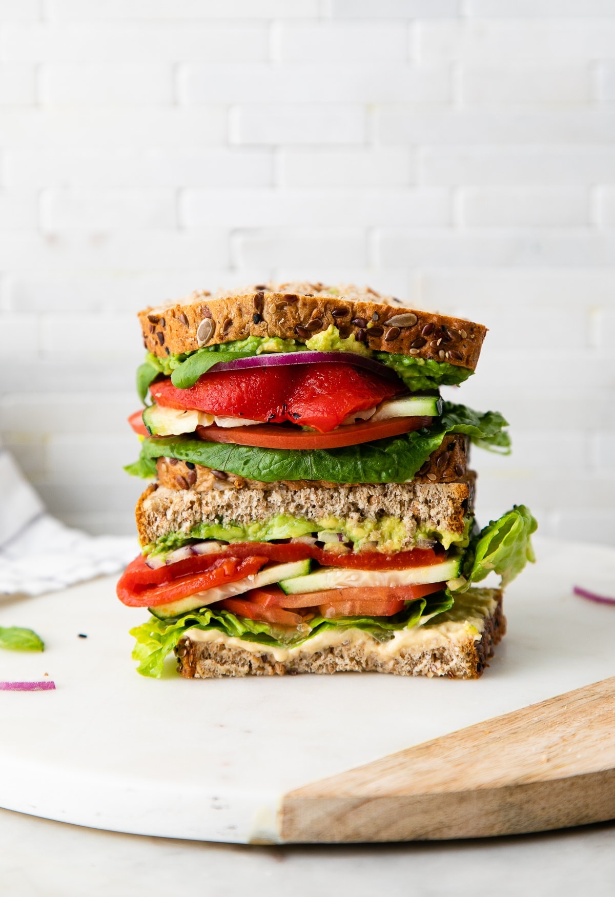 head on view of sliced and stacked mediterranean veggie sandwich with red peppers on a marble serving tray.