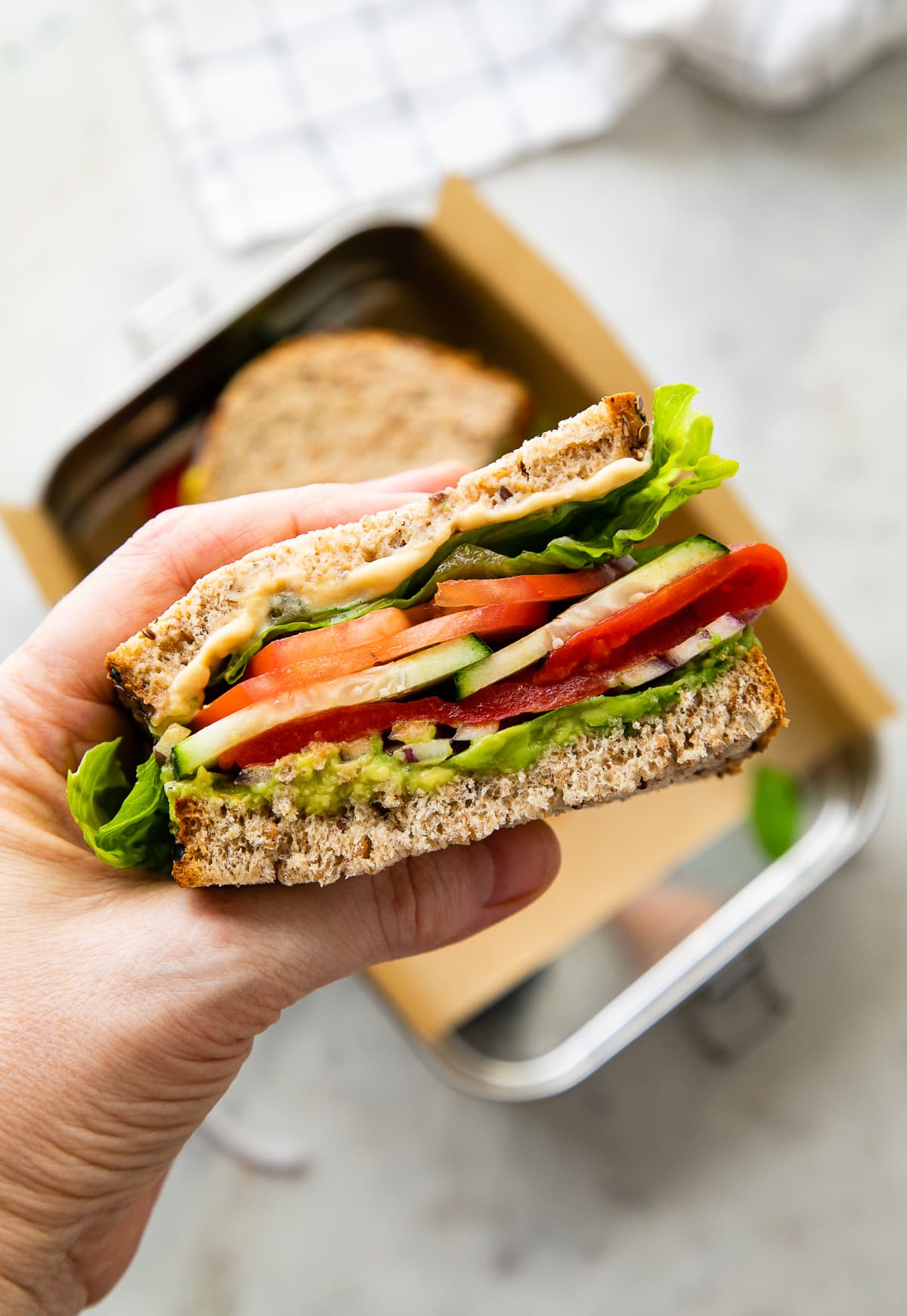 top down view of a hand holding a half of mediterranean veggie sandwich.