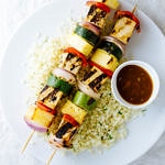 top down view of two grilled tofu skewers on a white plate with side of cauliflower rice and pineapple teriyaki sauce.