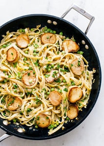 a top down view of skillet with alfredo noodles with king oyster mushrooms scallops and peas