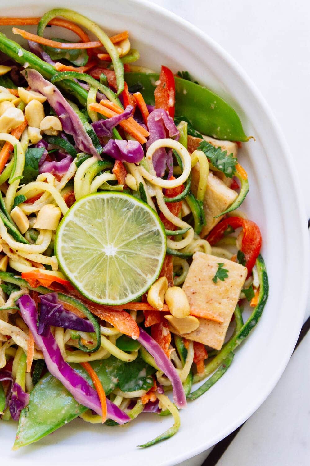 a white bowl filled with a serving of thai zucchini noodles and crispy tofu.