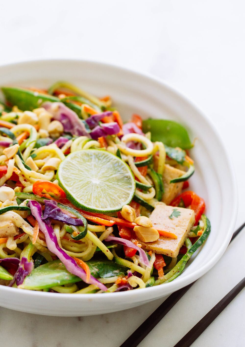 side angle view of a serving of thai zucchini noodles with crispy tofu in a white bowl.