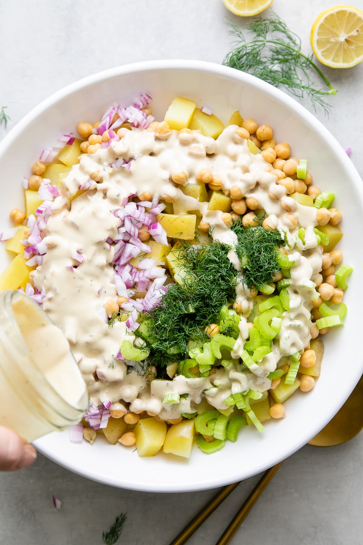 top down view showing the process of pouring dressing over dill potato salad.