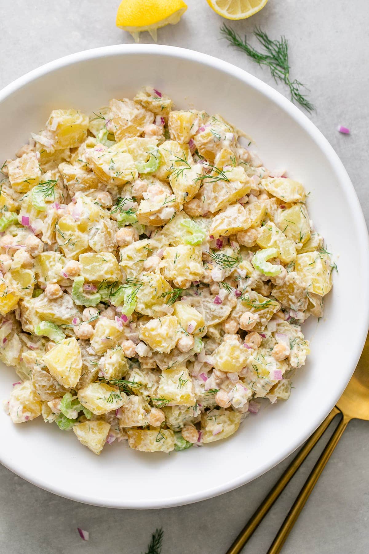 top down view of freshly made vegan dill potato salad in a white bowl with items surrounding.