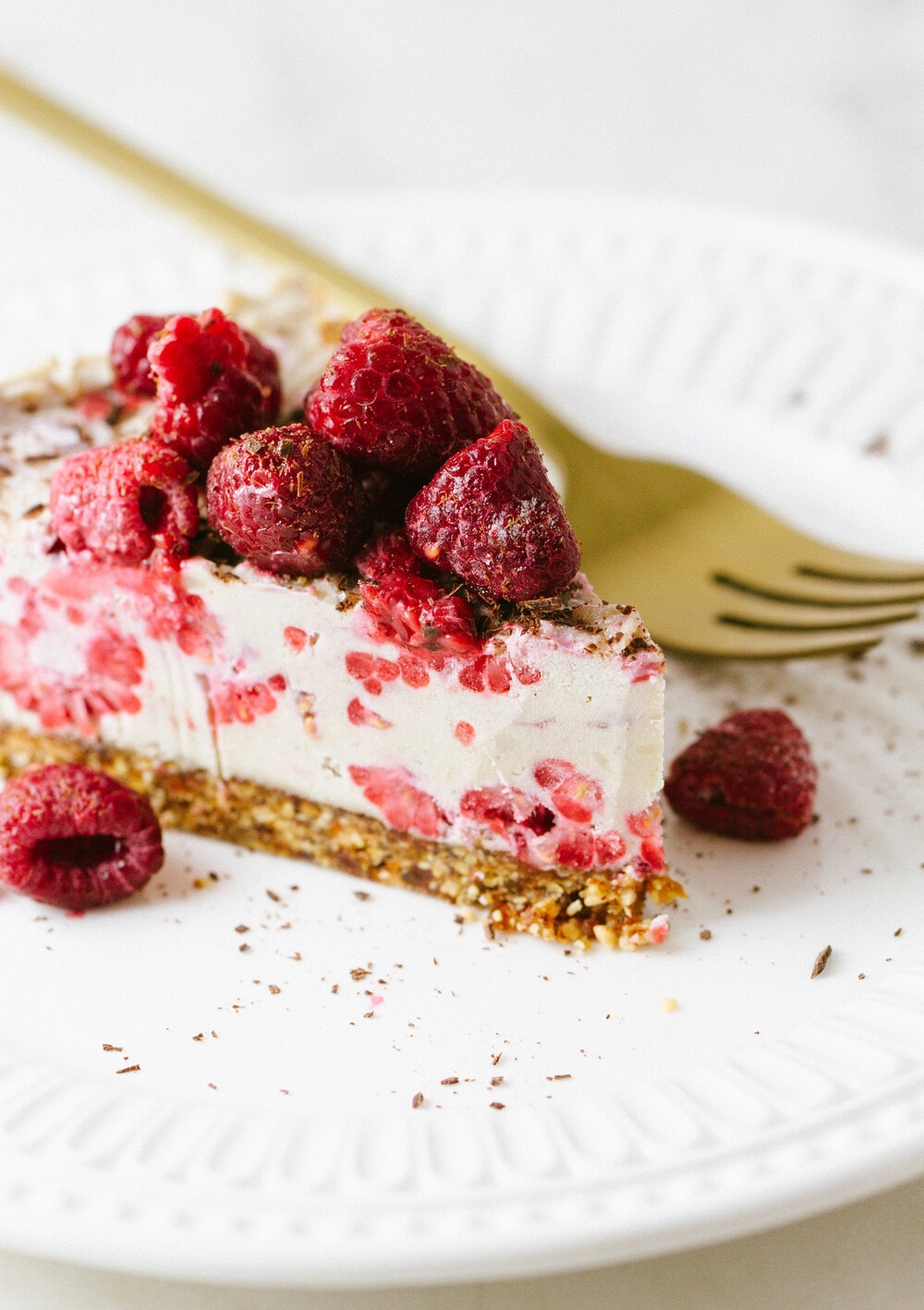 side angle view of a slice of vegan no bake raspberry vanilla cheesecake on a white plate with gold fork.